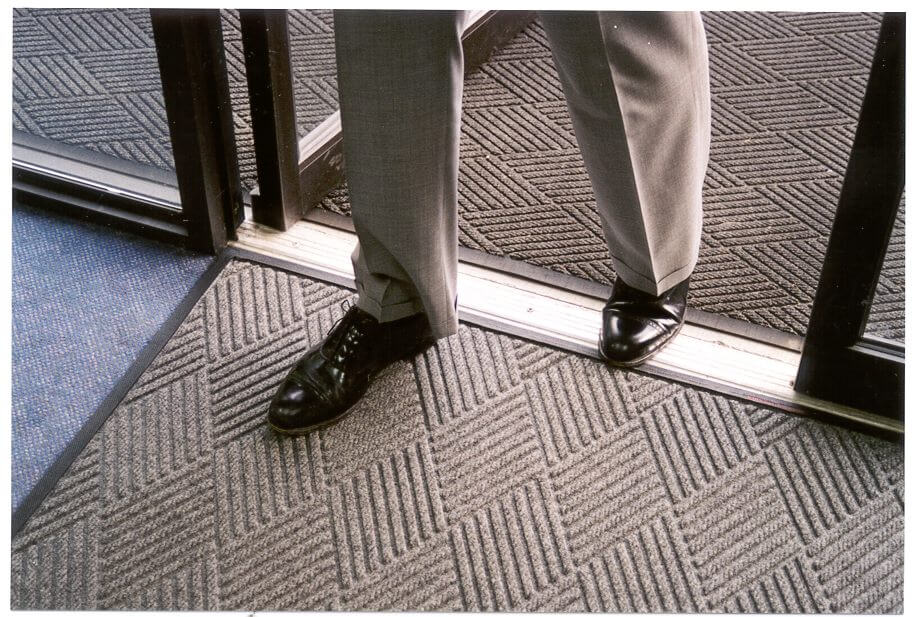 person stepping through door with a waterhog mat under foot